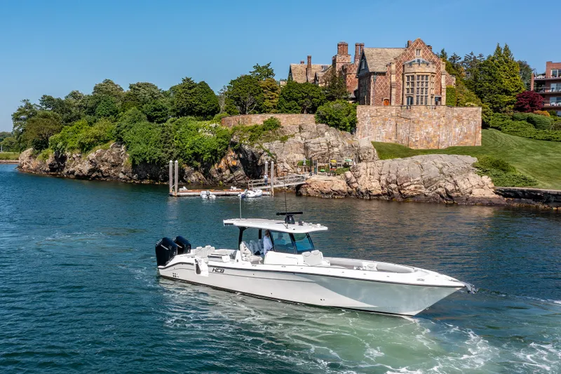  Yacht Photos Pics 2024 HCB 39 Speciale boat cruising near a historic mansion on a rocky shoreline.