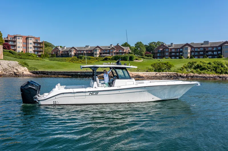  Yacht Photos Pics 2024 HCB 39 Speciale boat cruising near a scenic shoreline with buildings in the background.