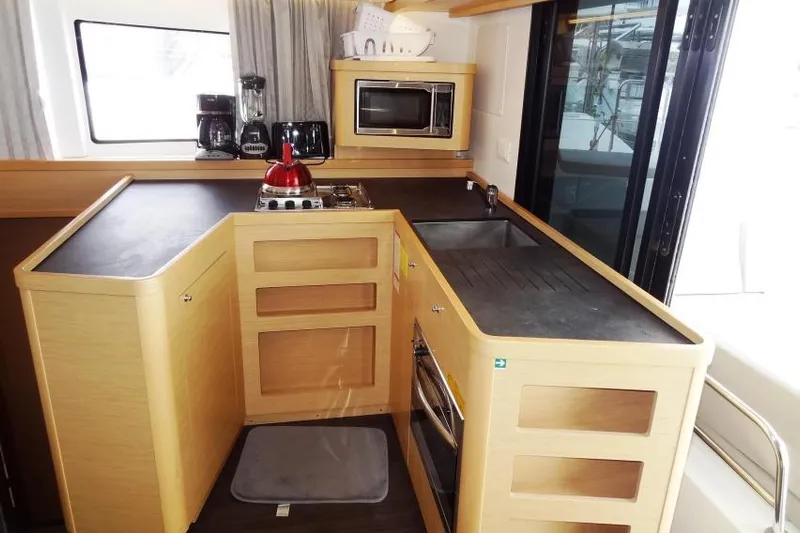 Pau Hana Yacht Photos Pics Modern kitchen interior of 2020 Lagoon 42 catamaran with appliances and wooden cabinetry.