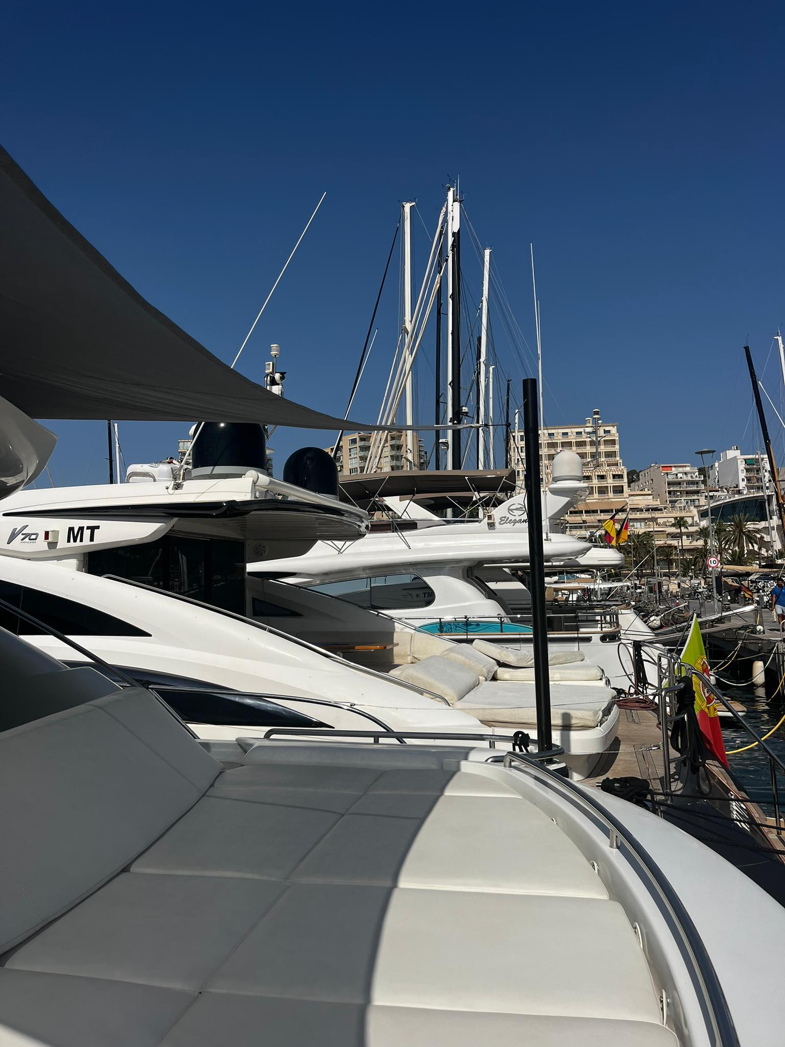 Luxury yachts docked at marina, featuring a 2004 Pershing 76 under clear blue sky.