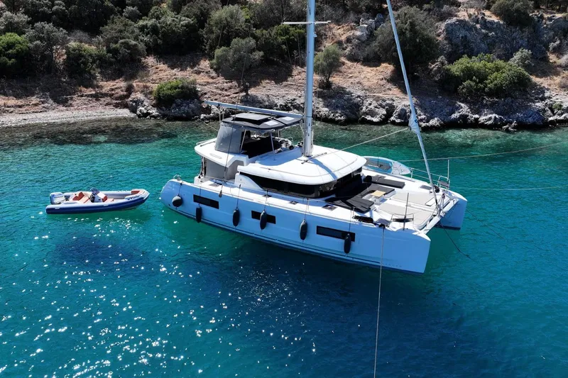  Yacht Photos Pics 2020 Lagoon 46 catamaran anchored in clear turquoise waters near a rocky shoreline.