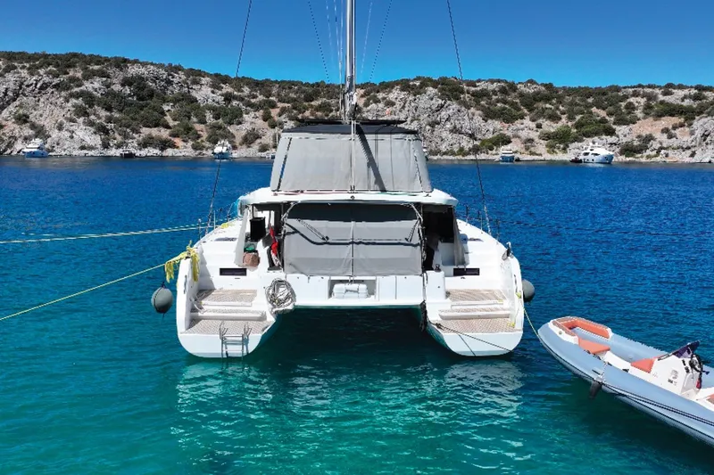  Yacht Photos Pics 2020 Lagoon 46 catamaran anchored in clear blue water, with scenic rocky coastline.