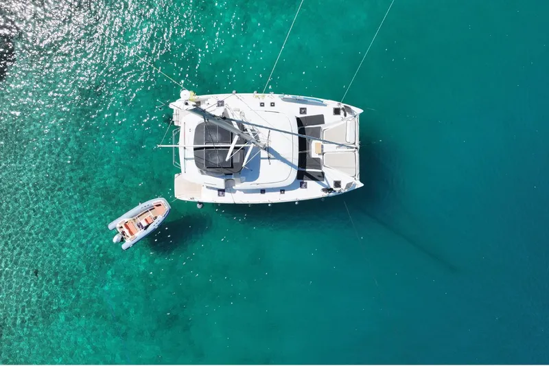  Yacht Photos Pics Aerial view of 2020 Lagoon 46 catamaran and dinghy on clear turquoise water.