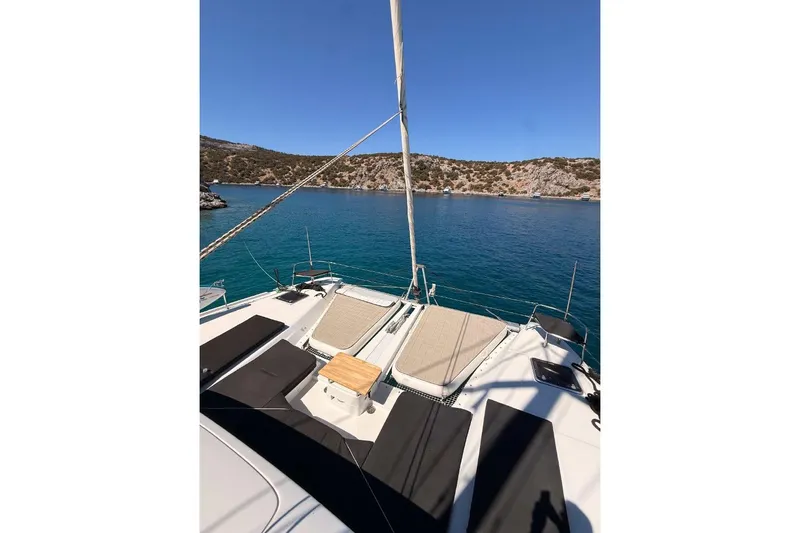  Yacht Photos Pics Lagoon 46 catamaran deck with sunbeds, overlooking serene blue waters and rocky coastline.