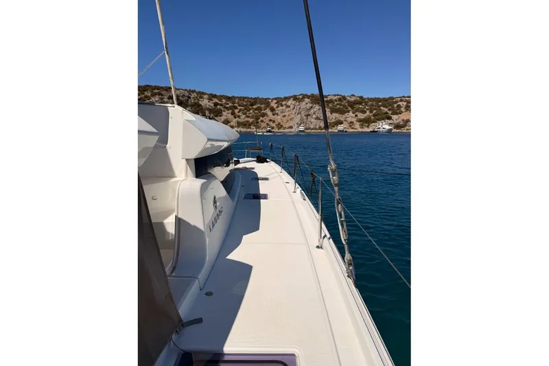  Yacht Photos Pics 2020 Lagoon 46 catamaran sailing in clear blue waters near rocky coastline.