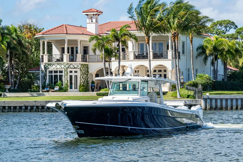 Yacht Photos Pics 2020 HCB 53 boat cruising near a luxurious waterfront mansion with palm trees.