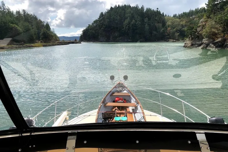 Outbound Yacht Photos Pics 1993 Symbol 55 Yachtfisher navigating scenic, forested waterway under cloudy sky.