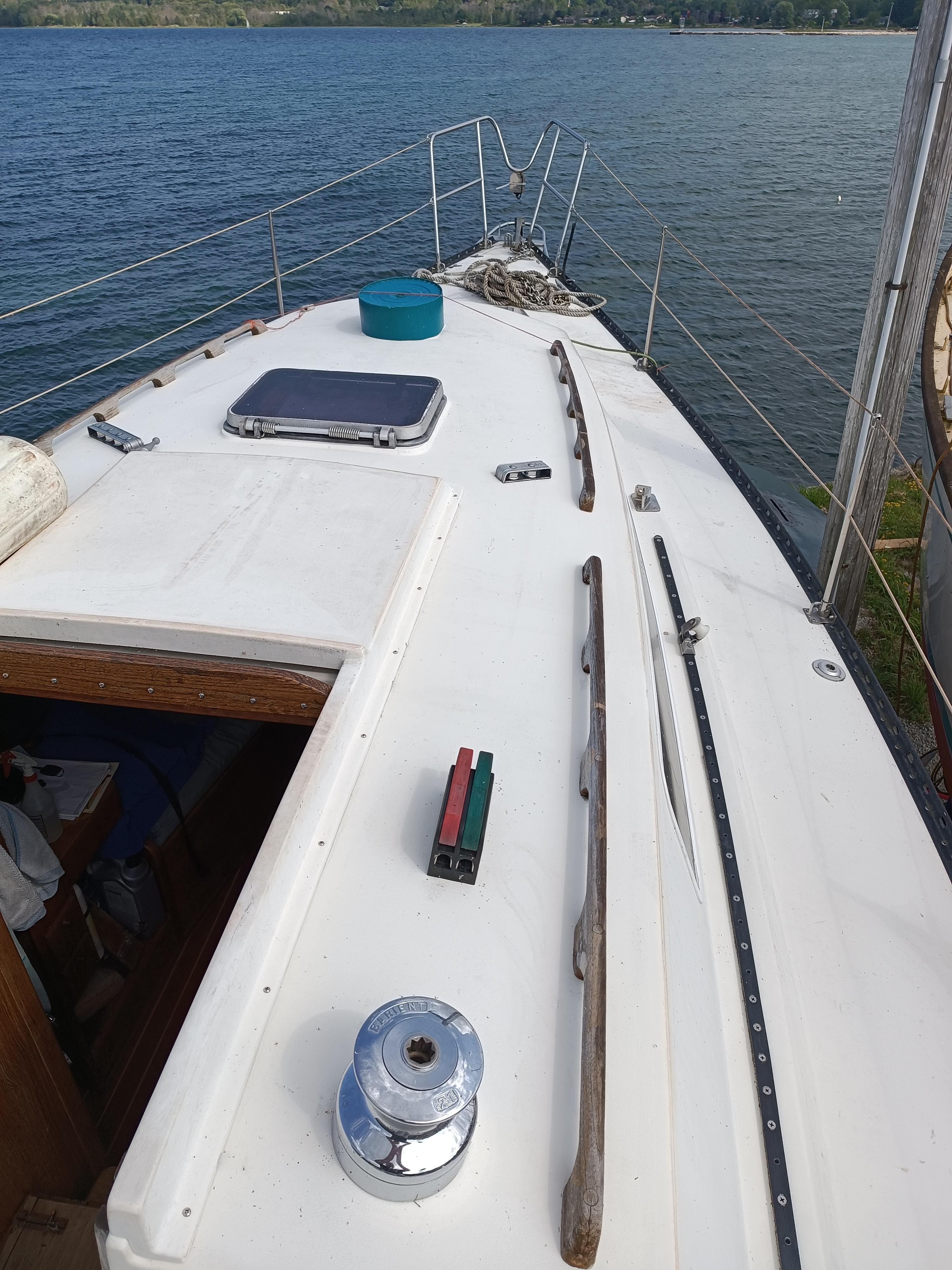 1988 Aloha 30 sailboat deck with winch, hatch, and railing, overlooking calm water.