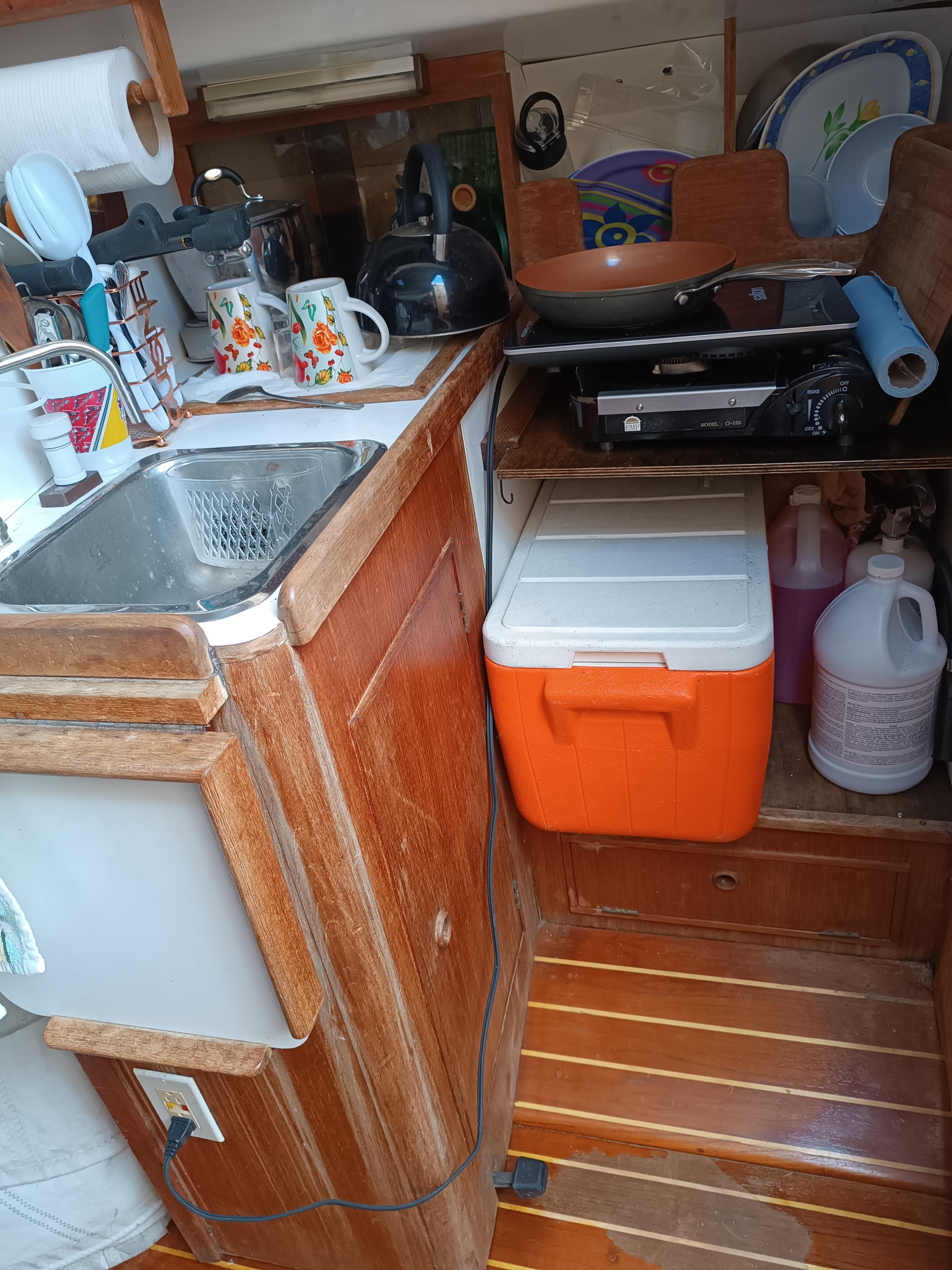 Compact kitchen area in a 1988 Aloha 30 sailboat with sink, cooler, and storage.