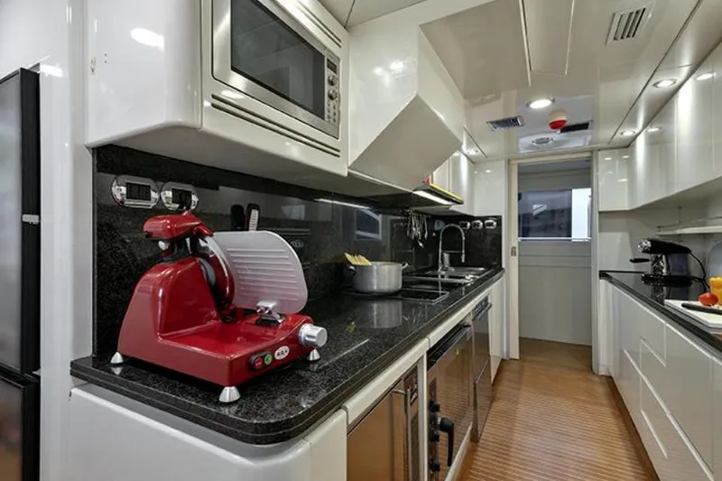 Don Ciro Yacht Photos Pics Luxurious yacht kitchen with modern appliances, featuring a red slicer and sleek black countertops. Benetti Sail Division 105, 2002.