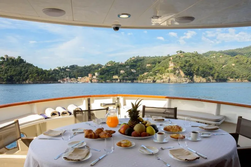 Don Ciro Yacht Photos Pics Luxury yacht dining setup on Benetti Sail Division 105, 2002, with scenic coastal view.