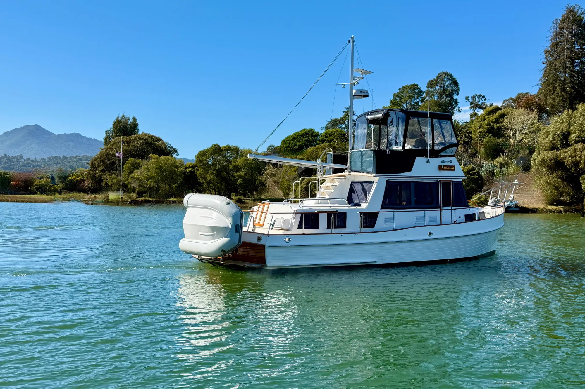 1997 Grand Banks Classic yacht on serene water with lush greenery and mountains in the background.