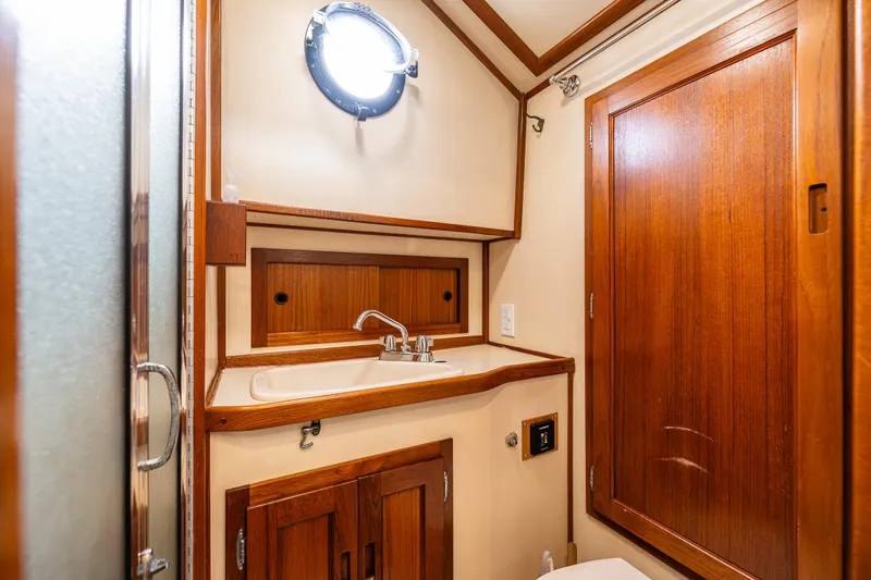 John Hunter Yacht Photos Pics Wood-accented bathroom in 2000 Nordic Tug 37 boat, featuring sink and porthole window.