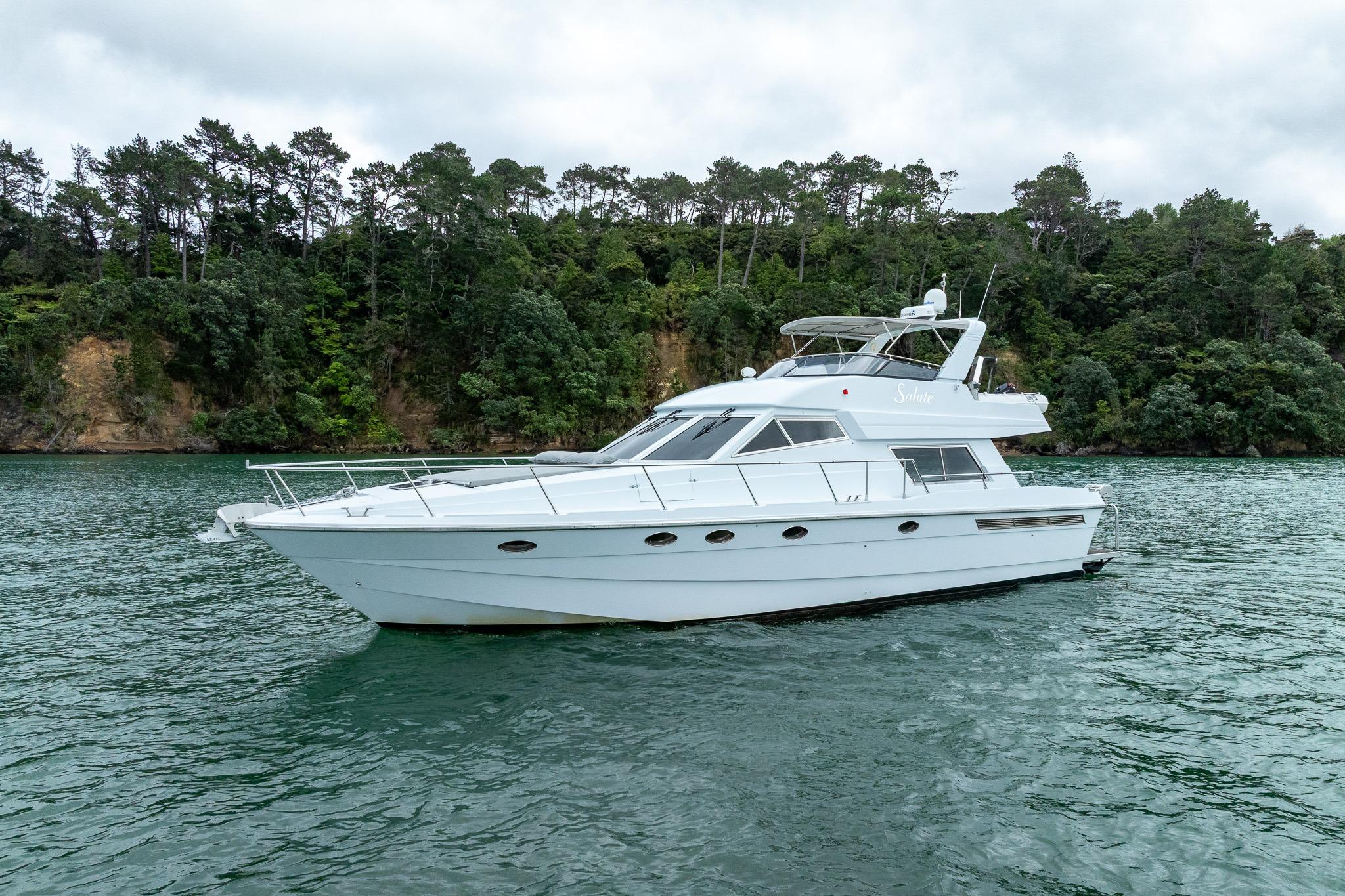 Luxury 1995 Comar Clanship 52 yacht on serene water with lush forest backdrop.