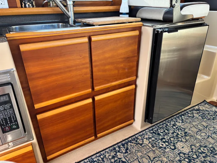 Y Knot Yacht Photos Pics 2017 Cutwater C-28 Deluxe kitchen with wooden cabinets, stainless steel fridge, and sink.