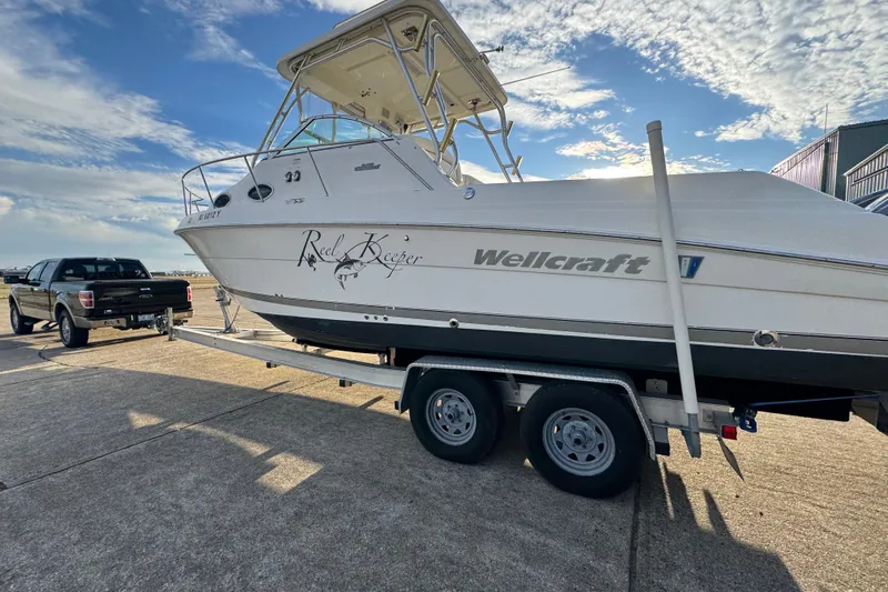  Yacht Photos Pics 2009 Wellcraft 270 Coastal O/B boat on trailer, parked beside a truck under a blue sky.