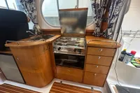Interior of 2001 Nimbus 345 Coupe boat kitchen with stove, sink, and wooden cabinetry.