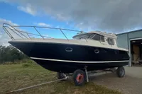 Nimbus 345 Coupe 2001 boat on trailer, parked outdoors near a building under cloudy sky.