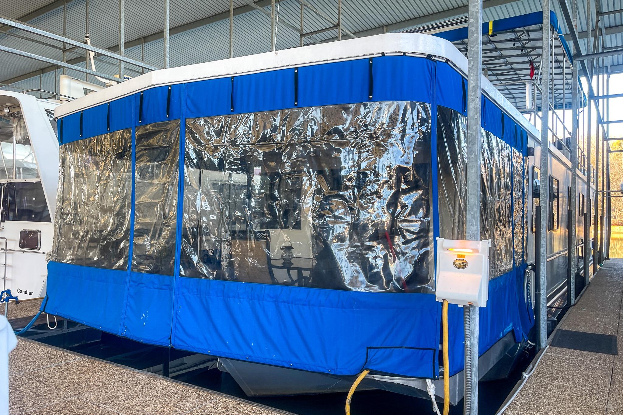 1996 Lakeview 66 x 16 Widebody Houseboat with blue and clear enclosure in a marina.