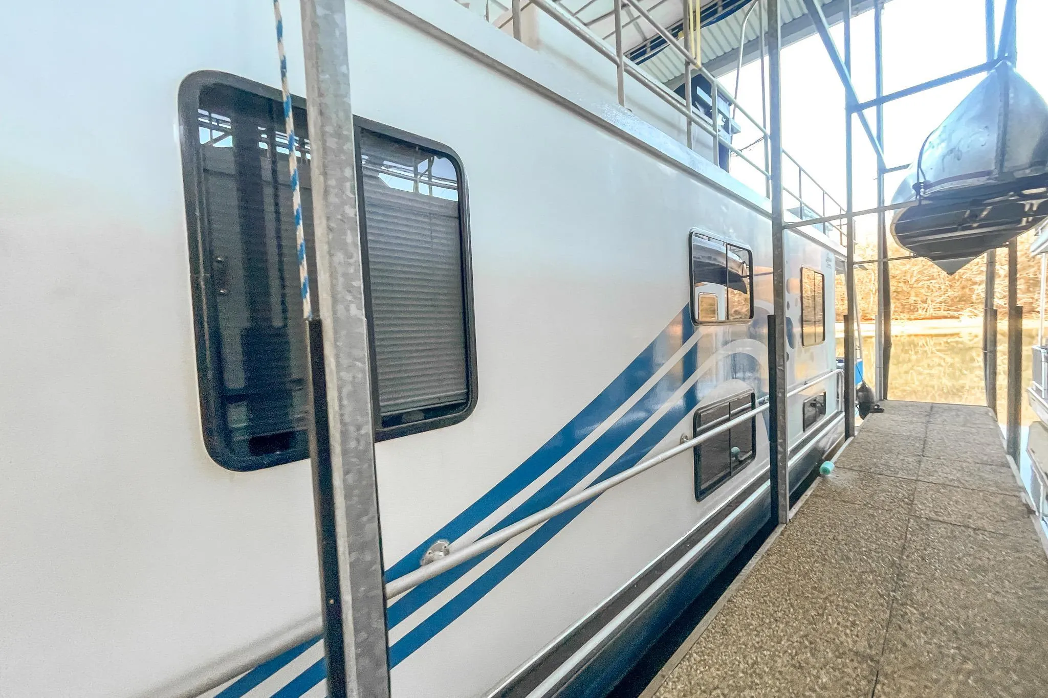 1996 Lakeview 66 x 16 Widebody Houseboat docked, featuring blue stripes and multiple windows.