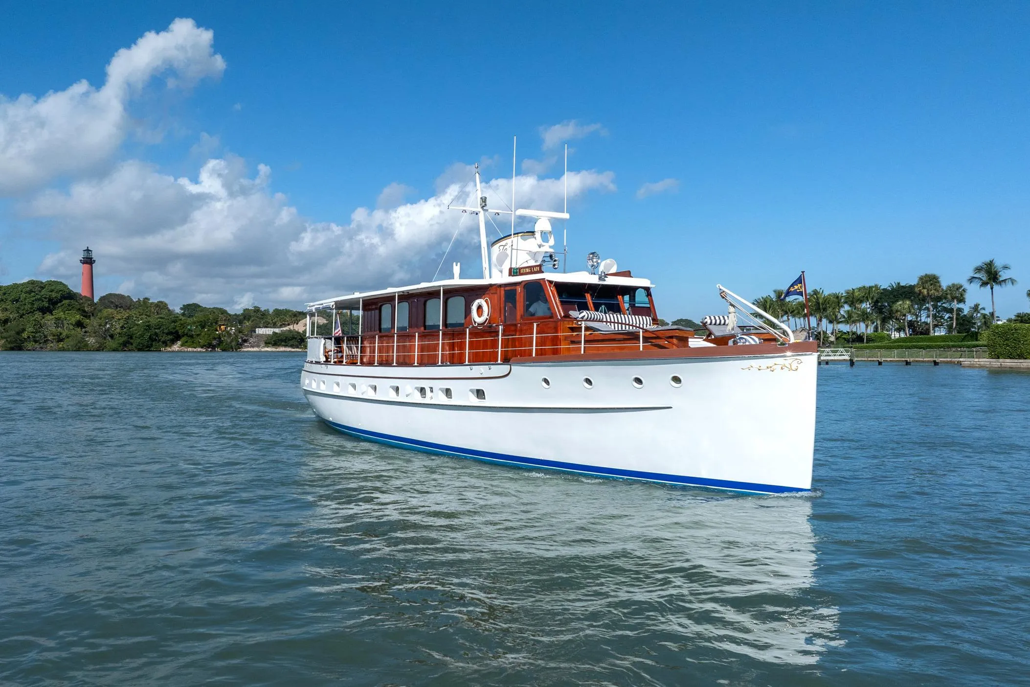 Classic 1937 Trumpy 58 yacht cruising on a sunny day near a lighthouse.