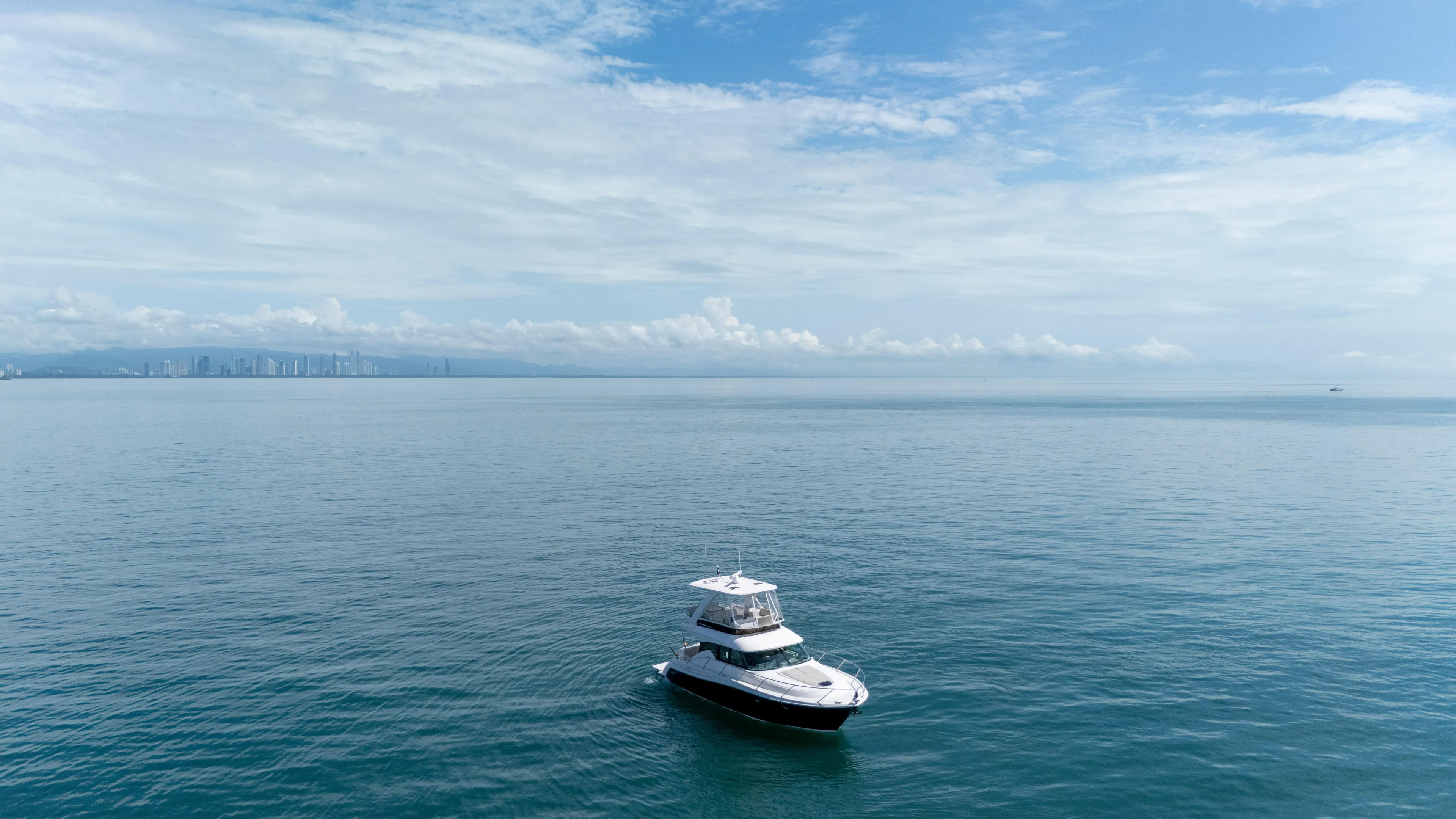  Yacht Photos Pics 2019 Tiara Yachts F44 Flybridge on calm ocean with distant city skyline.