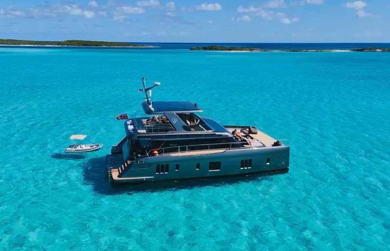  Yacht Photos Pics 2024 Sunreef 60 Eco yacht in turquoise waters, with a small boat nearby.