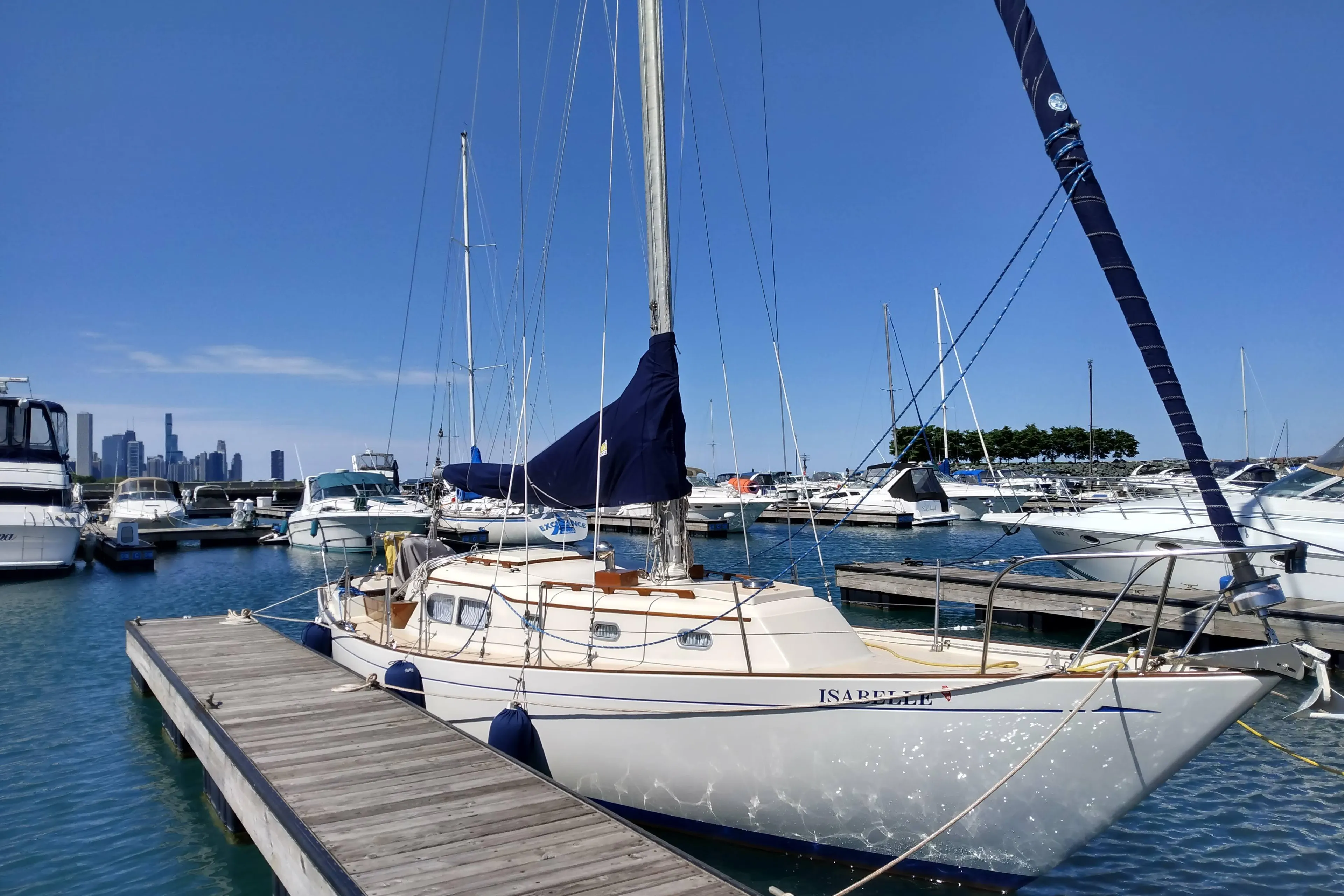 1969 Chris-Craft Apache 37 sailboat docked in marina with city skyline background.