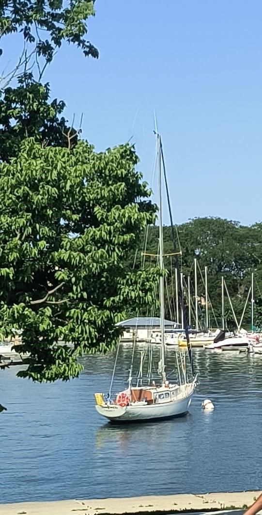 1969 Chris-Craft Apache 37 sailboat moored on a calm lake, surrounded by trees.