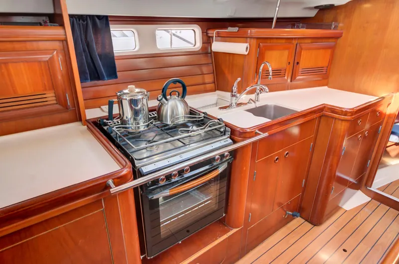 Phantom Yacht Photos Pics Luxurious 2002 Beneteau 473 yacht kitchen with stove, sink, and wooden cabinetry.