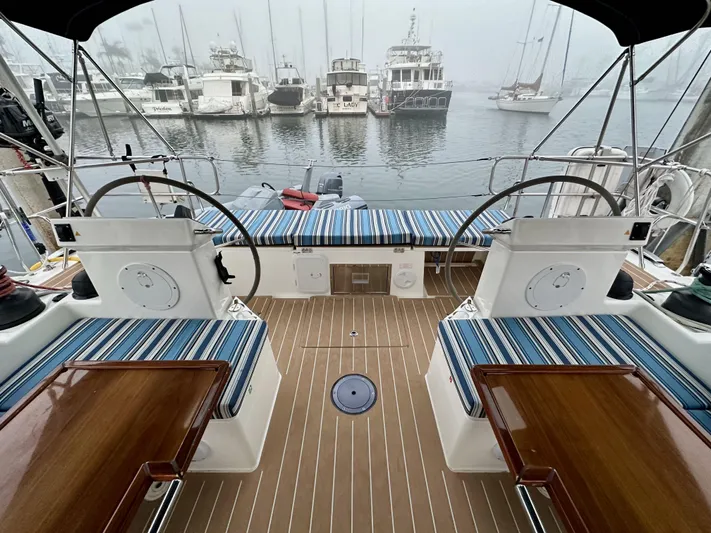 Painkiller Yacht Photos Pics Bavaria C50 yacht cockpit with dual steering wheels, striped seating, and marina view.