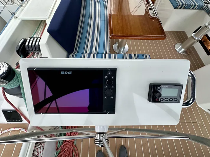 Painkiller Yacht Photos Pics Bavaria C50 yacht cockpit with navigation equipment, striped seating, and wooden table, 2020 model.