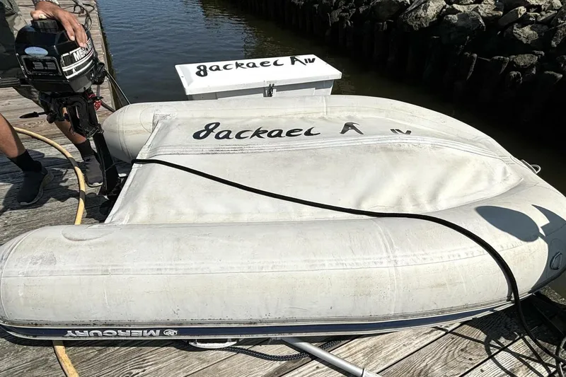  Yacht Photos Pics Inflatable boat with Mercury motor docked, labeled "Jackal A," near water and rocks.