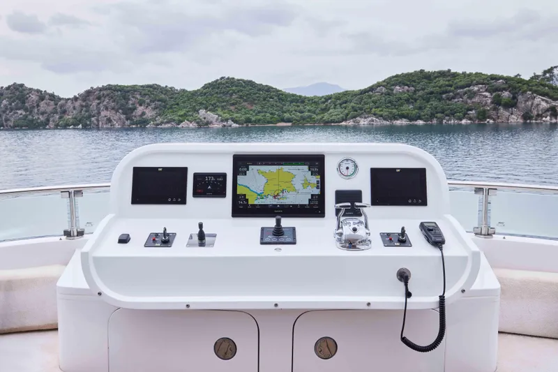 Aysha Yacht Photos Pics Helm of 2012 Timmerman 26 yacht with navigation equipment, overlooking serene waters and lush hills.