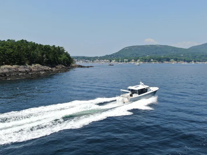 Artemis Yacht Photos Pics 2023 MJM 4 boat cruising on a scenic coastal waterway with lush green hills.
