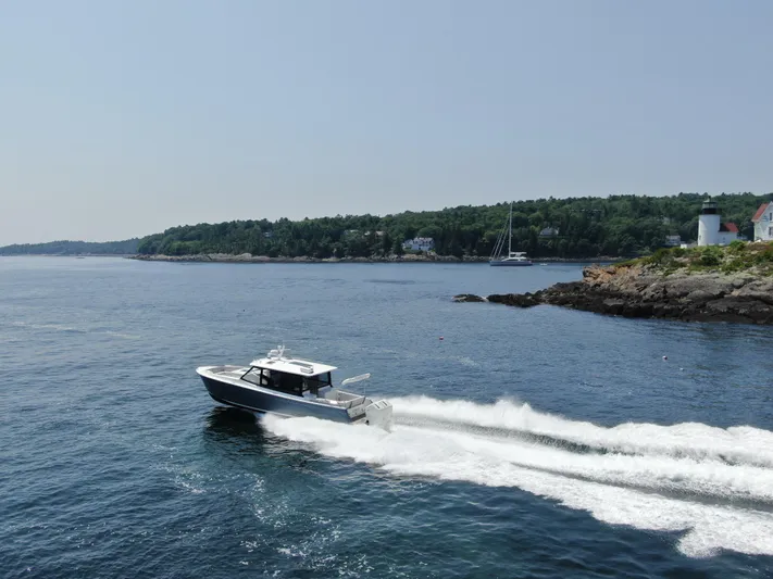 Artemis Yacht Photos Pics 2023 MJM 4 boat cruising near a rocky coastline with a lighthouse.