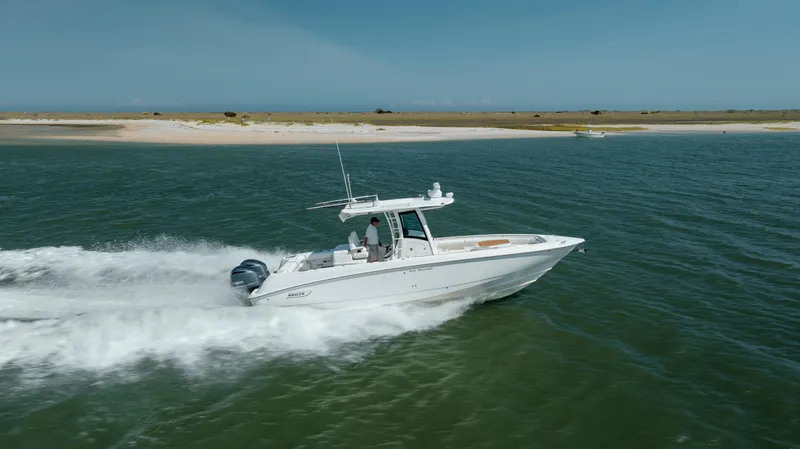  Yacht Photos Pics 2013 Boston Whaler 320 Outrage cruising on open water near a sandy shoreline.