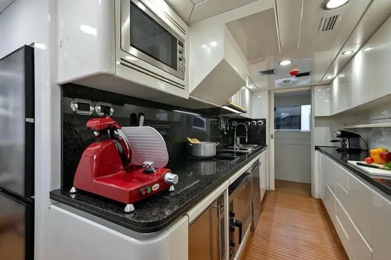  Yacht Photos Pics Luxurious yacht kitchen with modern appliances, featuring a red slicer and sleek black countertops. Benetti Sail Division 105, 2002.