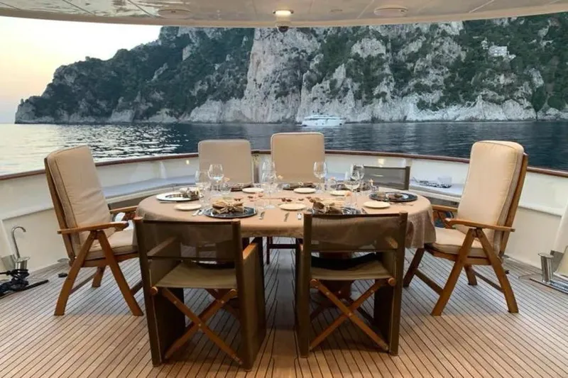  Yacht Photos Pics Luxury dining setup on 2002 Benetti Sail Division 105 yacht, scenic coastal backdrop.
