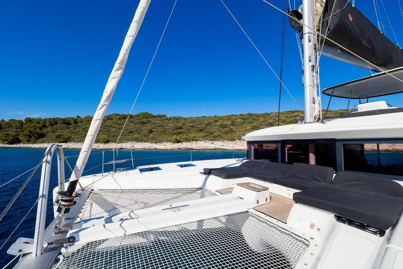 Catwalk Yacht Photos Pics 2023 Lagoon LAGOON 51 catamaran with spacious deck, sailing near a scenic coastline.