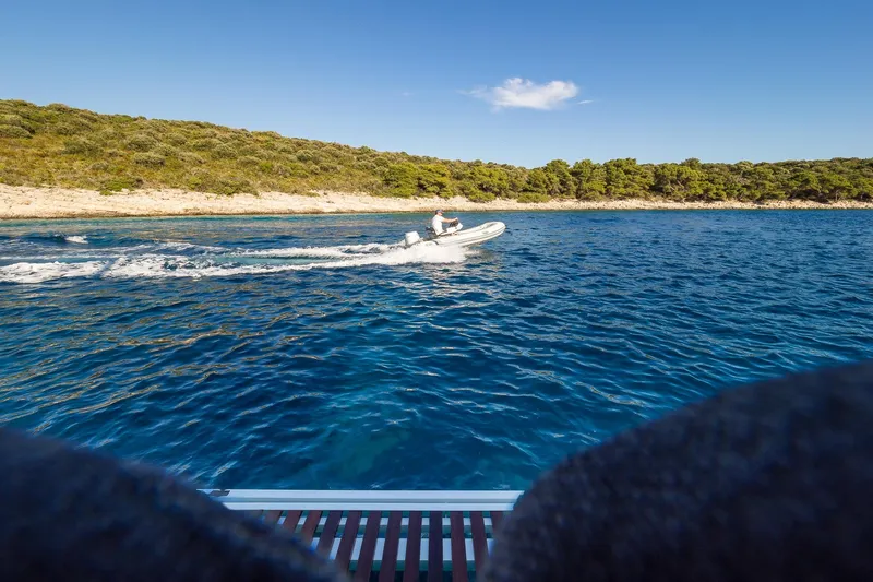 Catwalk Yacht Photos Pics Person riding a small boat on blue water near a forested shoreline, viewed from a Lagoon 51 yacht.