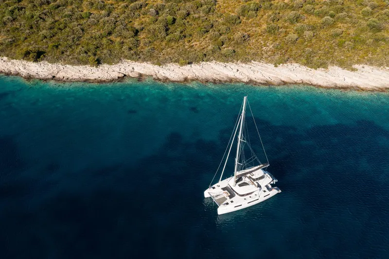 Catwalk Yacht Photos Pics Aerial view of 2023 Lagoon 51 catamaran sailing near a rocky coastline.