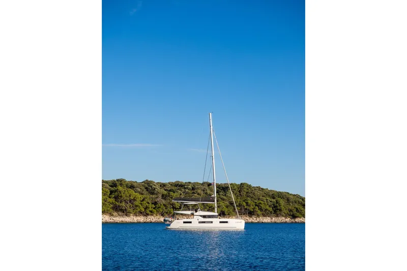 Catwalk Yacht Photos Pics 2023 Lagoon 51 yacht sailing near a lush, green coastline under a clear blue sky.
