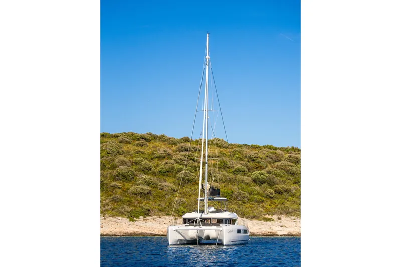 Catwalk Yacht Photos Pics 2023 Lagoon 51 catamaran anchored near a lush, green hillside under a clear blue sky.