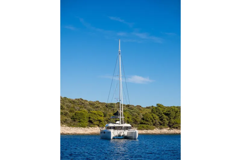 Catwalk Yacht Photos Pics 2023 Lagoon 51 catamaran anchored near a scenic, tree-lined coastline.