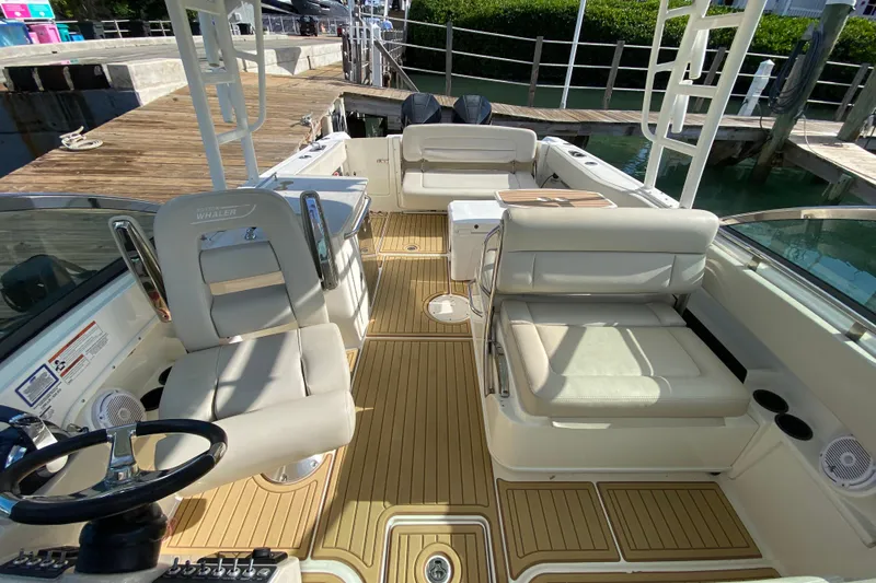  Yacht Photos Pics 2019 Boston Whaler 270 Vantage boat interior with seating and steering wheel, docked by wooden pier.