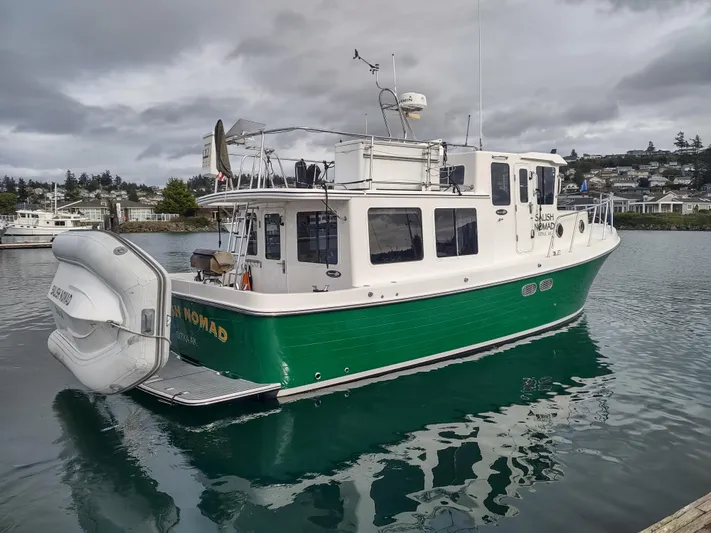 Salish Nomad Yacht Photos Pics 2007 American Tug 34 in green, docked on a calm waterway under cloudy skies.