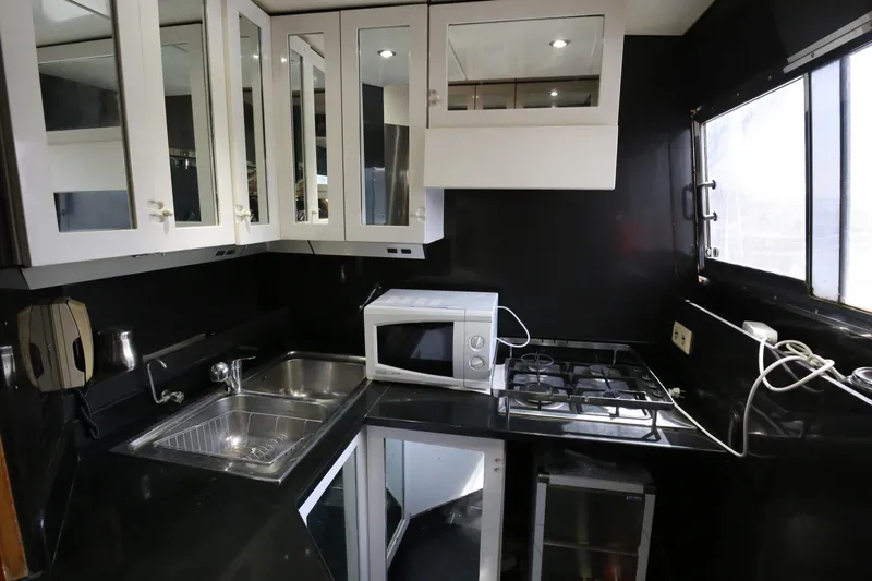  Yacht Photos Pics Compact kitchen in a 1990 Sanlorenzo 80 yacht with modern appliances and sleek black countertops.