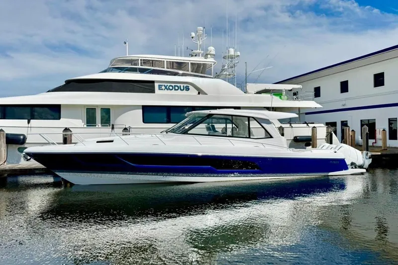 Yacht Photos Pics 2026 Intrepid 50 yacht docked beside a larger vessel, reflecting on calm water.
