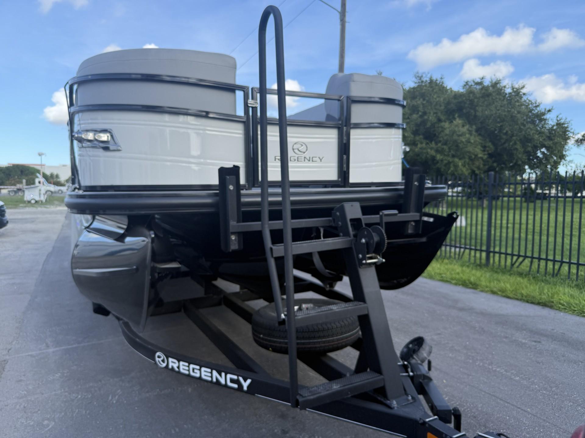 2024 Regency 250 DL3 pontoon boat on trailer, parked outdoors under blue sky.